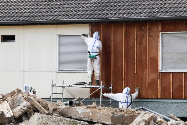 Professionals in protective suits carefully remove asbestos from a wall, ensuring safety and compliance with trusted asbestos removal services.